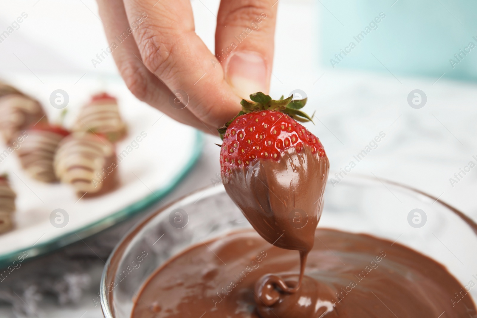 Photo of Woman dipping ripe strawberry into bowl with melted chocolate, closeup