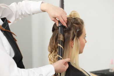 Hair styling. Hairdresser curling woman's hair in salon, closeup