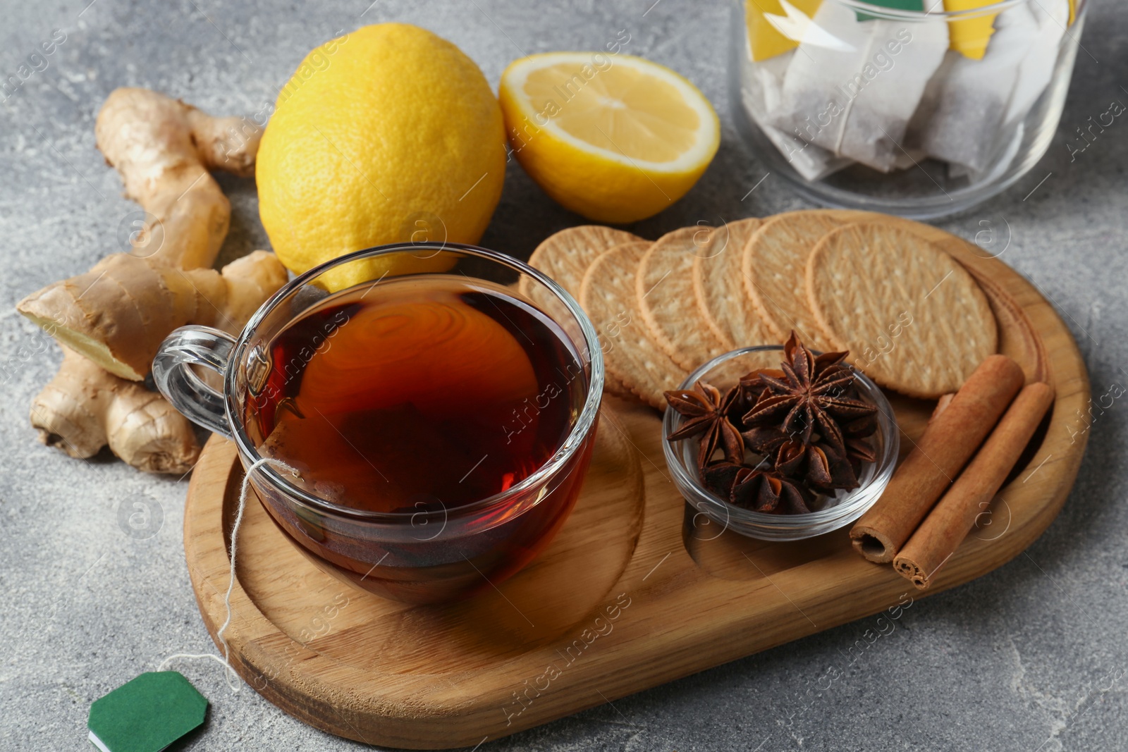 Photo of Tea bags, cup of hot drink, cookies and ingredients on light grey table