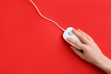 Photo of Woman using modern wired optical mouse on red background, top view. Space for text