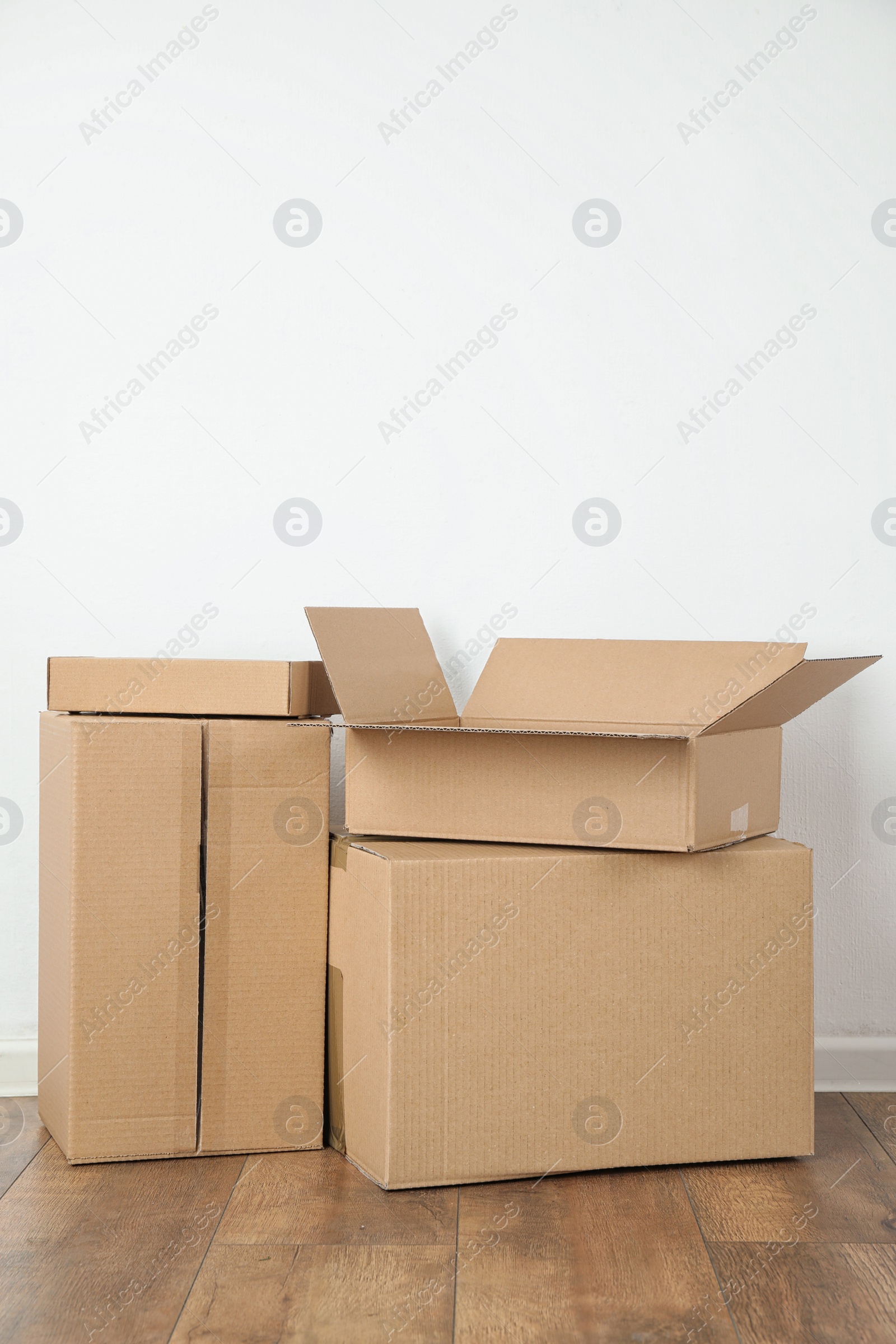 Photo of Pile of cardboard boxes near white wall indoors. Space for text