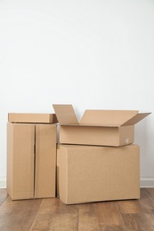 Photo of Pile of cardboard boxes near white wall indoors. Space for text