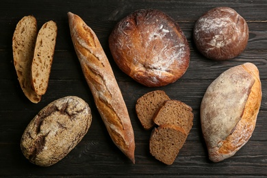 Photo of Different kinds of fresh bread on black wooden table, flat lay