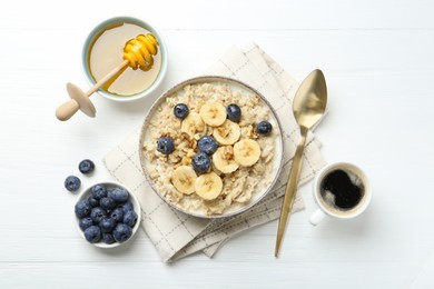 Tasty oatmeal with banana, blueberries, walnuts and honey served in bowl on white wooden table, flat lay