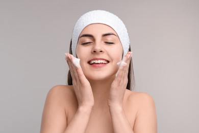 Photo of Young woman with headband washing her face on light grey background