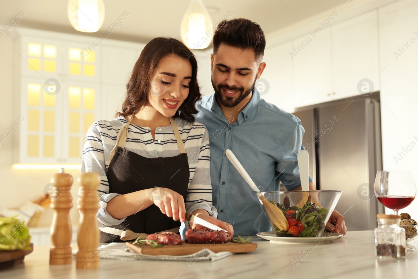 Photo of Lovely young couple cooking meat together in kitchen