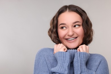 Photo of Smiling woman with dental braces in warm sweater on grey background. Space for text