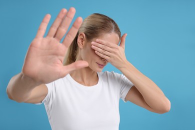 Photo of Embarrassed woman covering face on light blue background