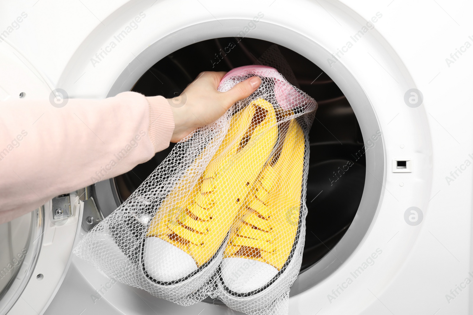 Photo of Woman putting stylish sneakers into washing machine, closeup