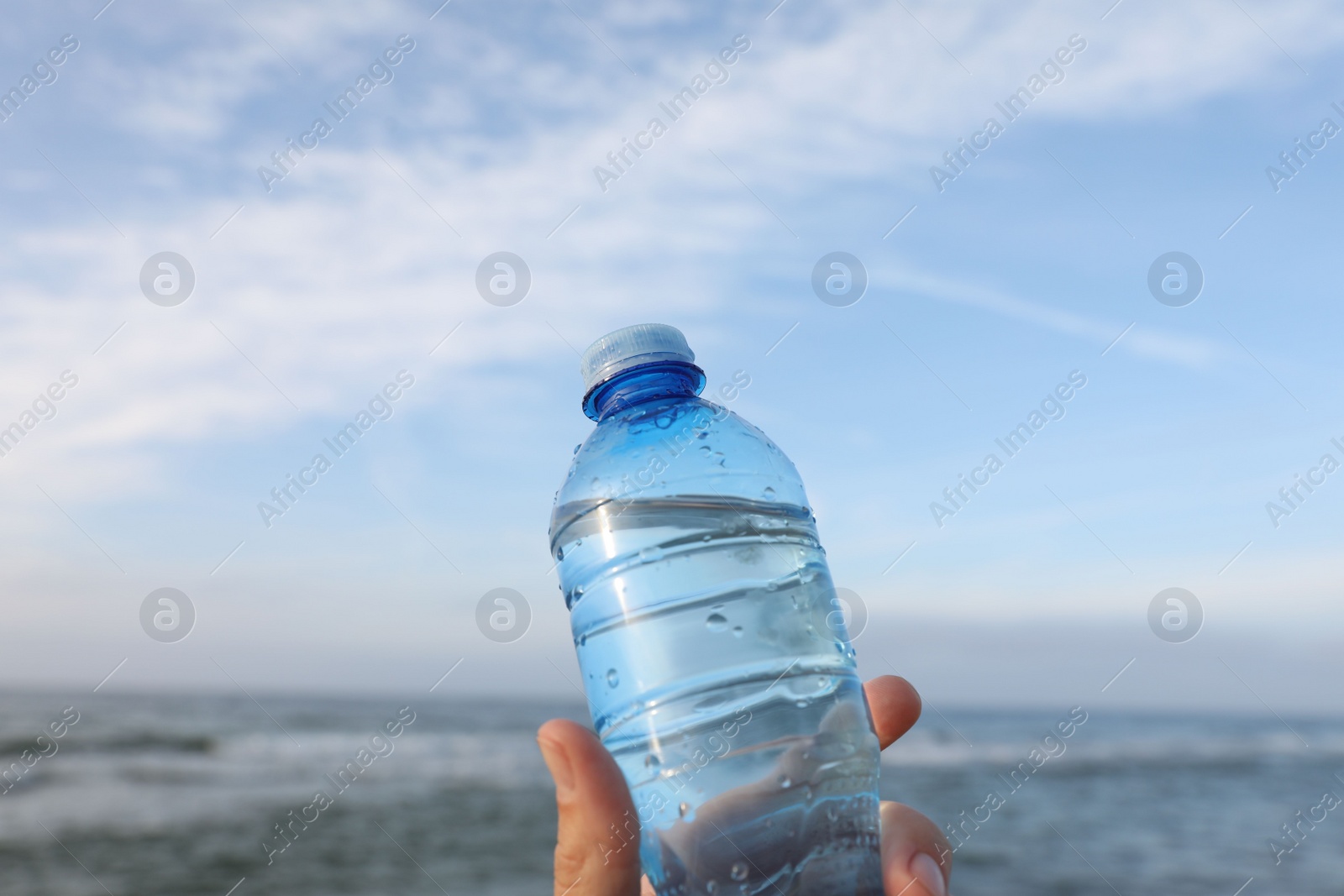 Photo of Woman holding plastic bottle with water near sea, closeup