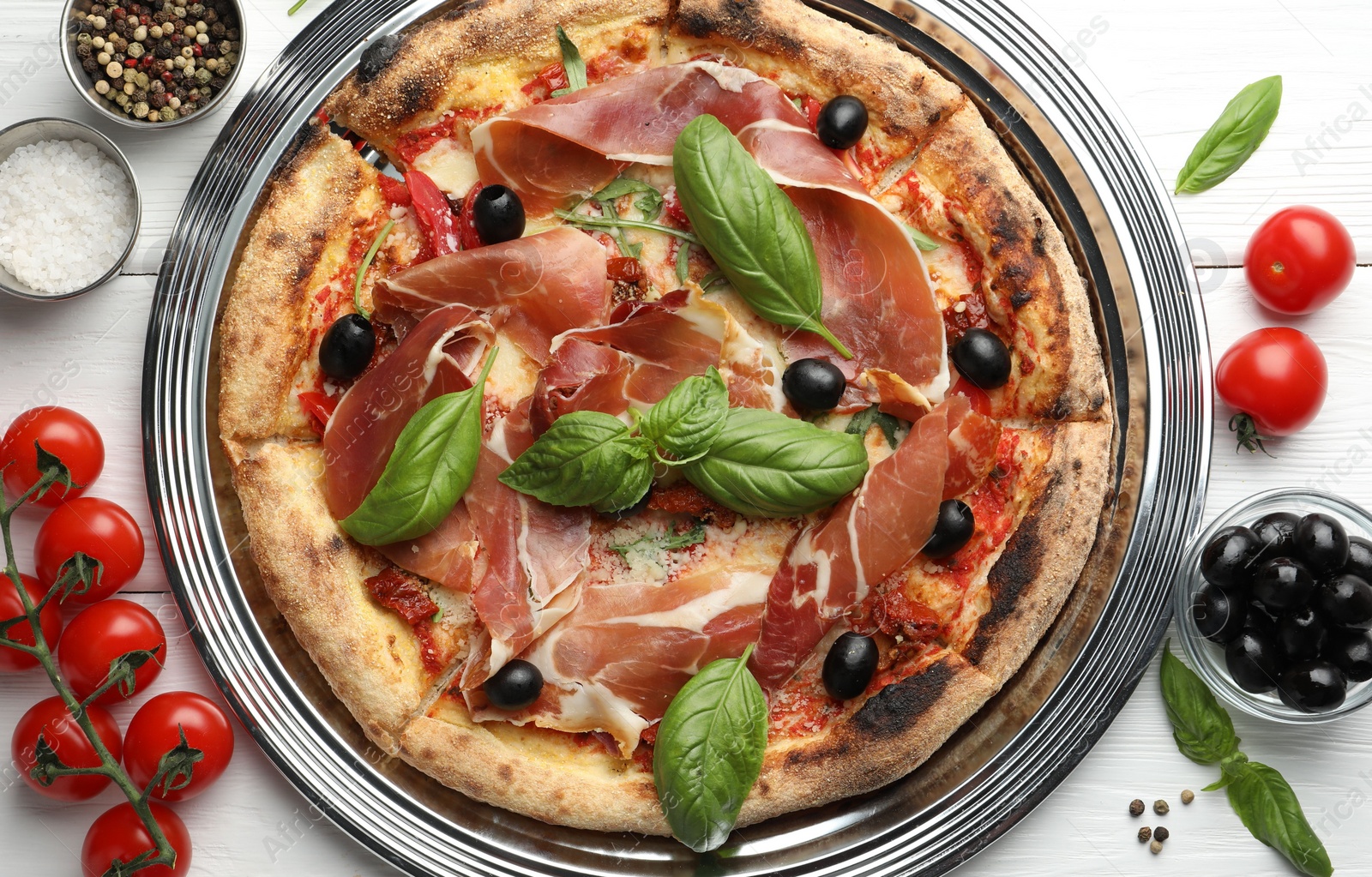 Photo of Tasty pizza with cured ham, olives, tomatoes and basil on white wooden table, flat lay