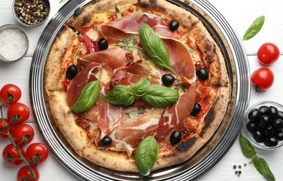 Tasty pizza with cured ham, olives, tomatoes and basil on white wooden table, flat lay