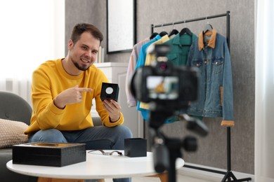 Photo of Smiling fashion blogger pointing at wristwatch while recording video at home