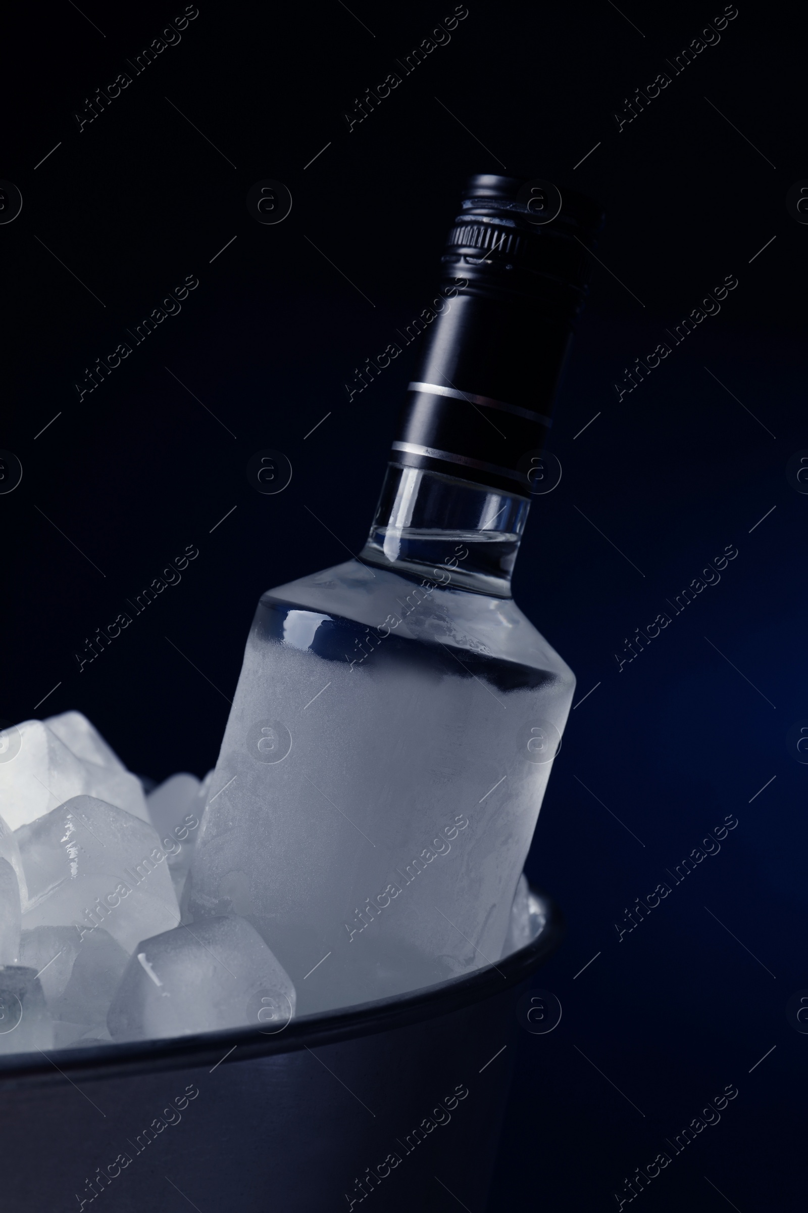 Photo of Bottle of vodka in metal bucket with ice on dark background