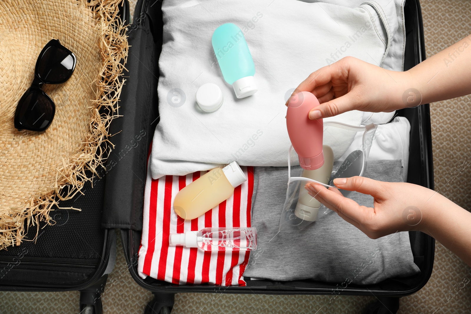 Photo of Woman putting small bottle with personal care product into plastic bag, closeup. Cosmetic travel kit