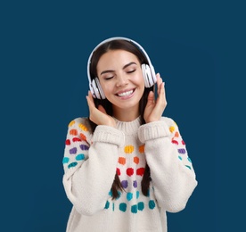 Young woman listening to music with headphones on dark blue background, space for text