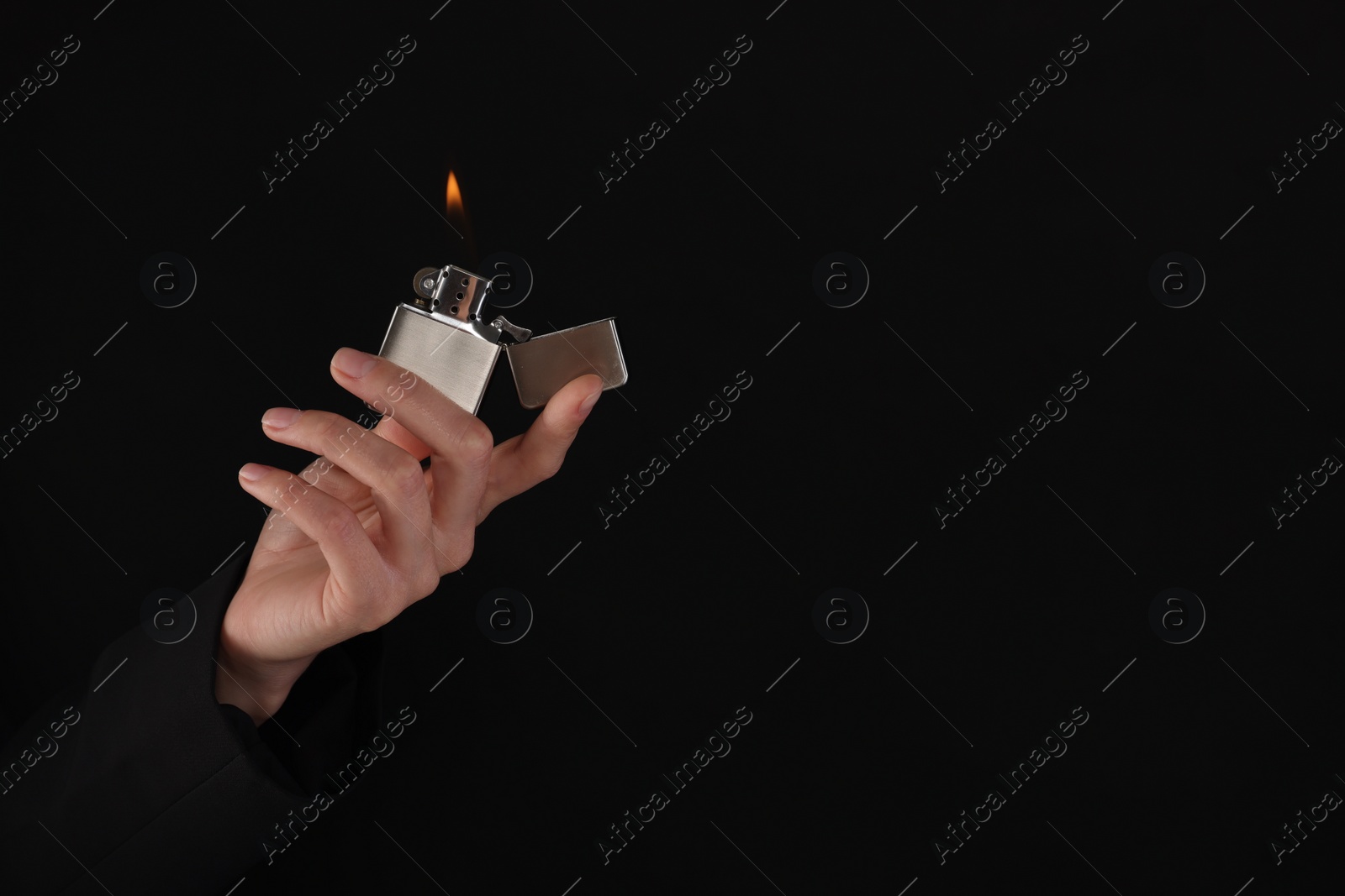 Photo of Woman holding lighter with burning flame on black background, closeup. Space for text