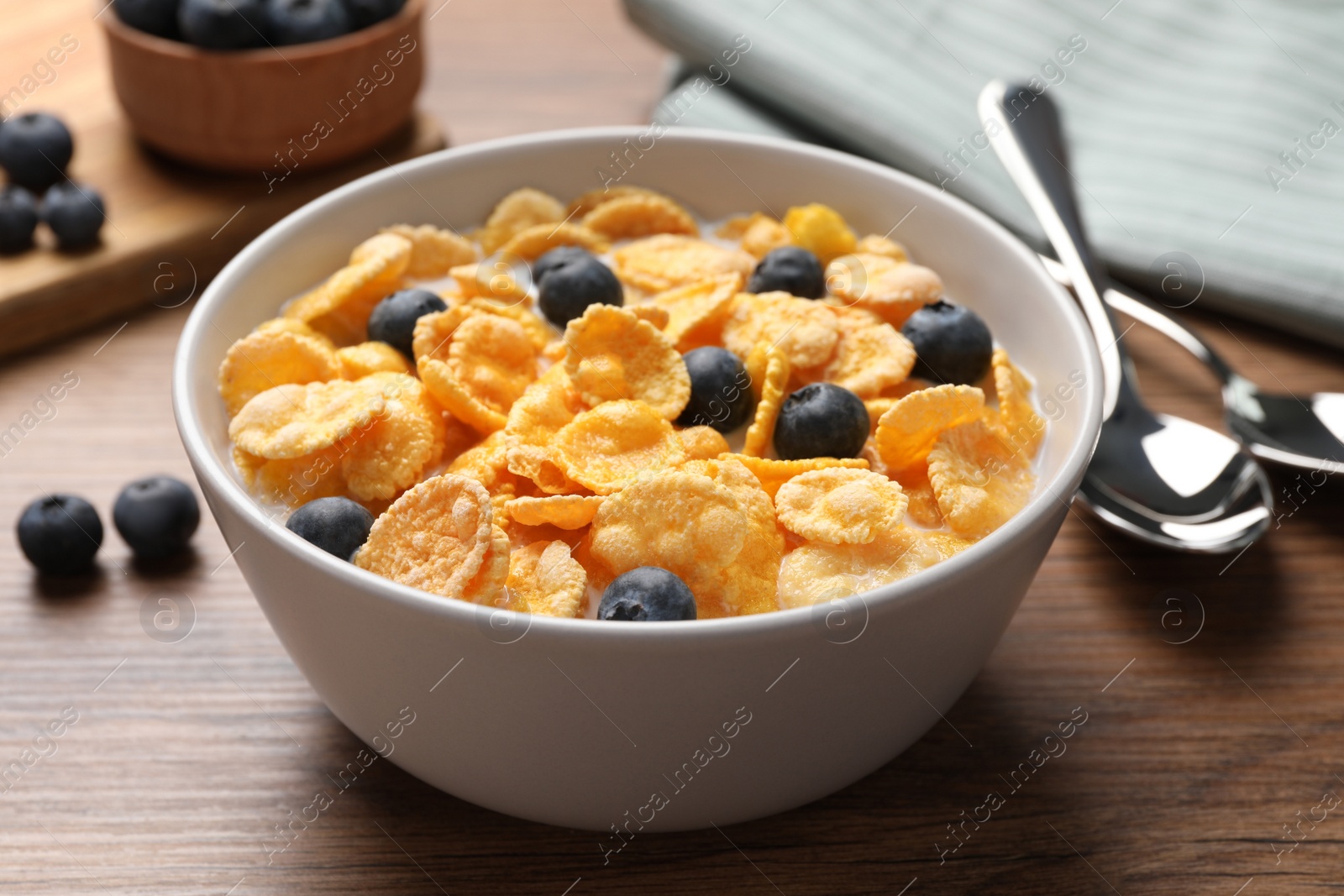 Photo of Bowl of tasty crispy corn flakes with milk and blueberries on wooden table, closeup