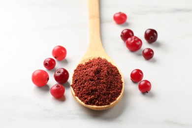 Photo of Dried cranberry powder in spoon and fresh berries on white marble table, closeup