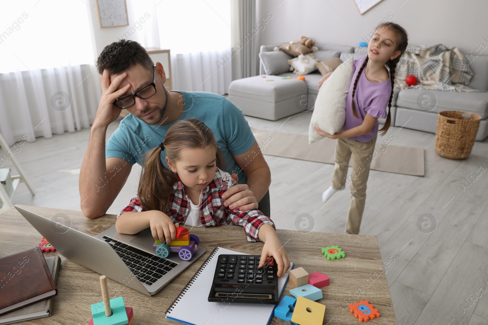 Photo of Children disturbing stressed man in living room. Working from home during quarantine