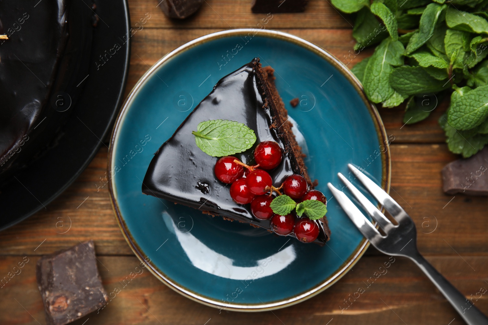 Photo of Piece of tasty homemade chocolate cake with berries and mint on wooden table, flat lay