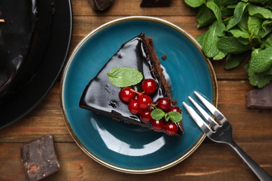 Photo of Piece of tasty homemade chocolate cake with berries and mint on wooden table, flat lay