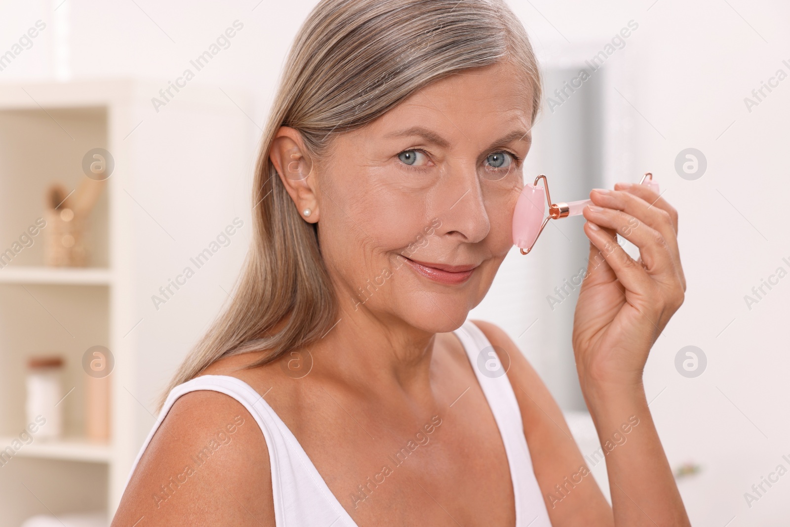 Photo of Woman massaging her face with rose quartz roller in bathroom