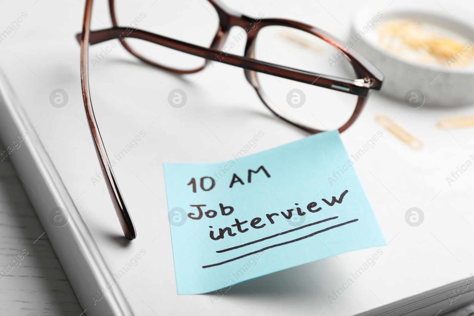 Photo of Notebook with reminder note about job interview and glasses on table, closeup