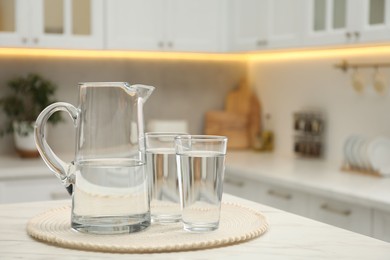 Photo of Jug and glasses with clear water on white table in kitchen, space for text