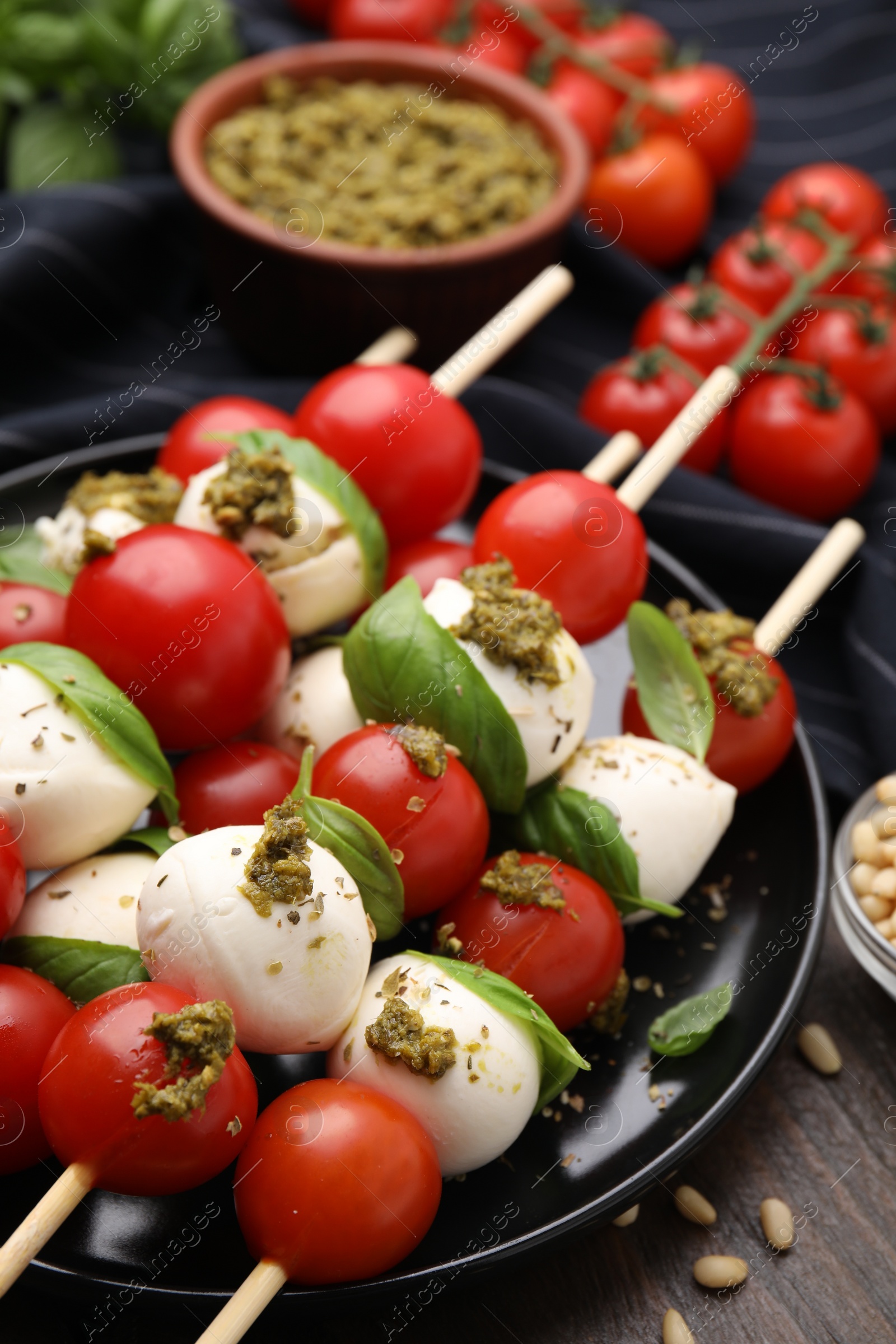 Photo of Caprese skewers with tomatoes, mozzarella balls, basil and pesto sauce on table, closeup
