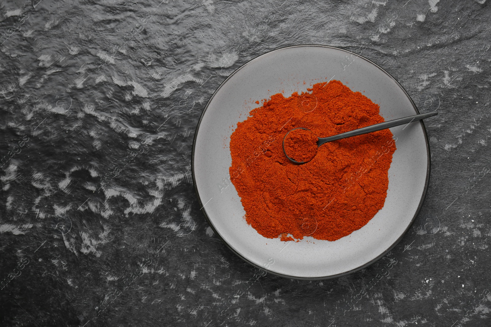 Photo of Plate of aromatic paprika on black textured table, top view. Space for text
