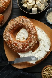 Photo of Delicious bagel with tofu cream cheese and soy beans on black wooden table, flat lay