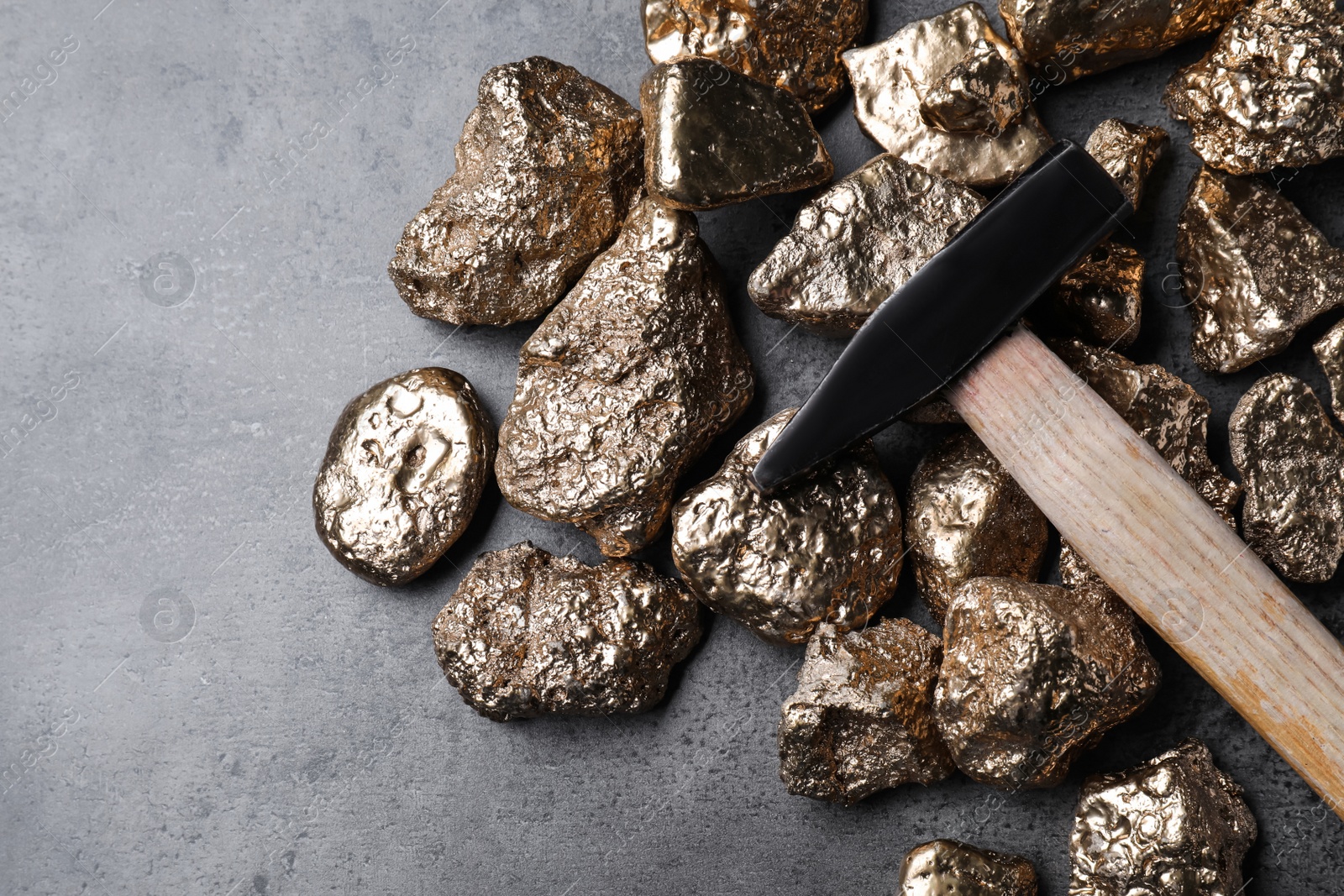 Photo of Gold nuggets and hammer on grey table, flat lay