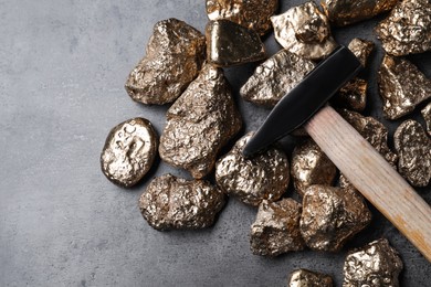 Gold nuggets and hammer on grey table, flat lay