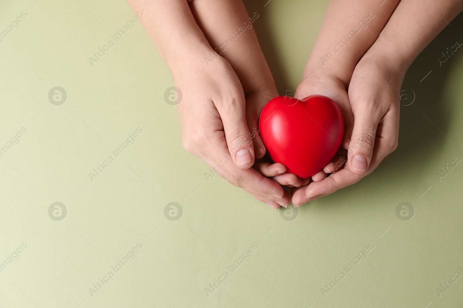 Photo of Mother and her child holding red decorative heart on light green background, top view. Space for text