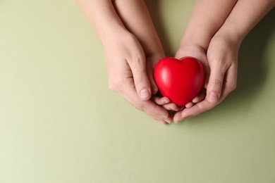 Photo of Mother and her child holding red decorative heart on light green background, top view. Space for text