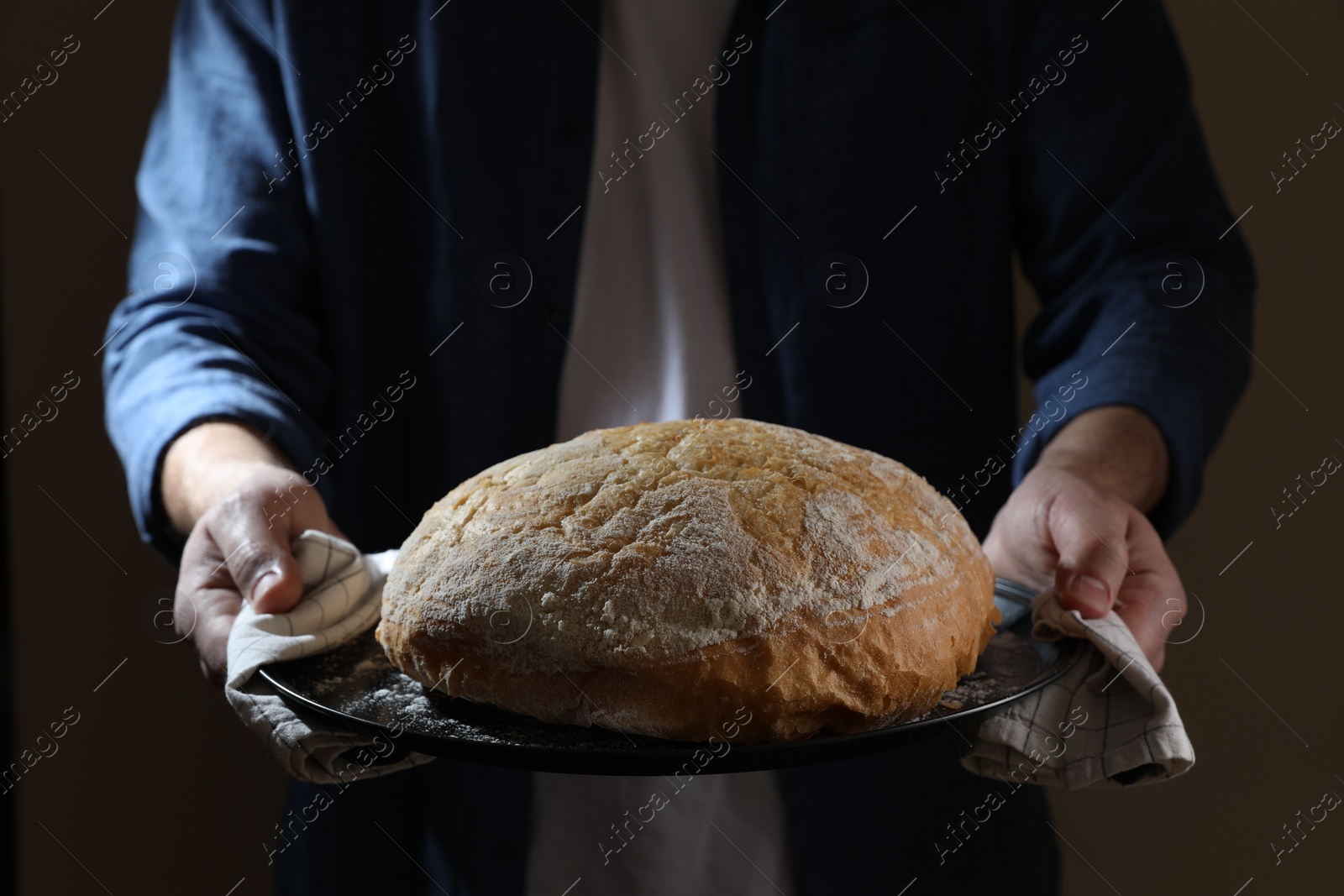 Photo of Man holding loaf of fresh bread on dark background, closeup