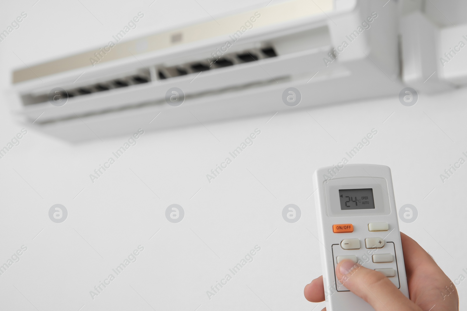 Photo of Man operating air conditioner with remote control indoors