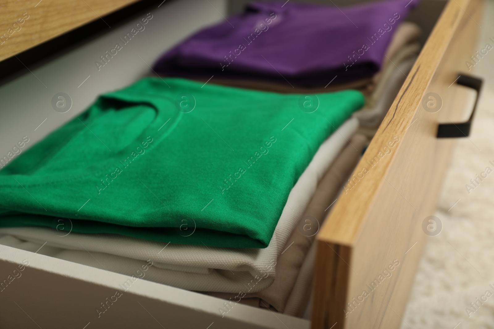 Photo of Stacks of different folded shirts in drawer, closeup. Organizing clothes