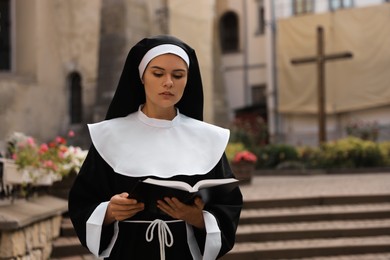 Photo of Young nun reading Bible near building outdoors. Space for text
