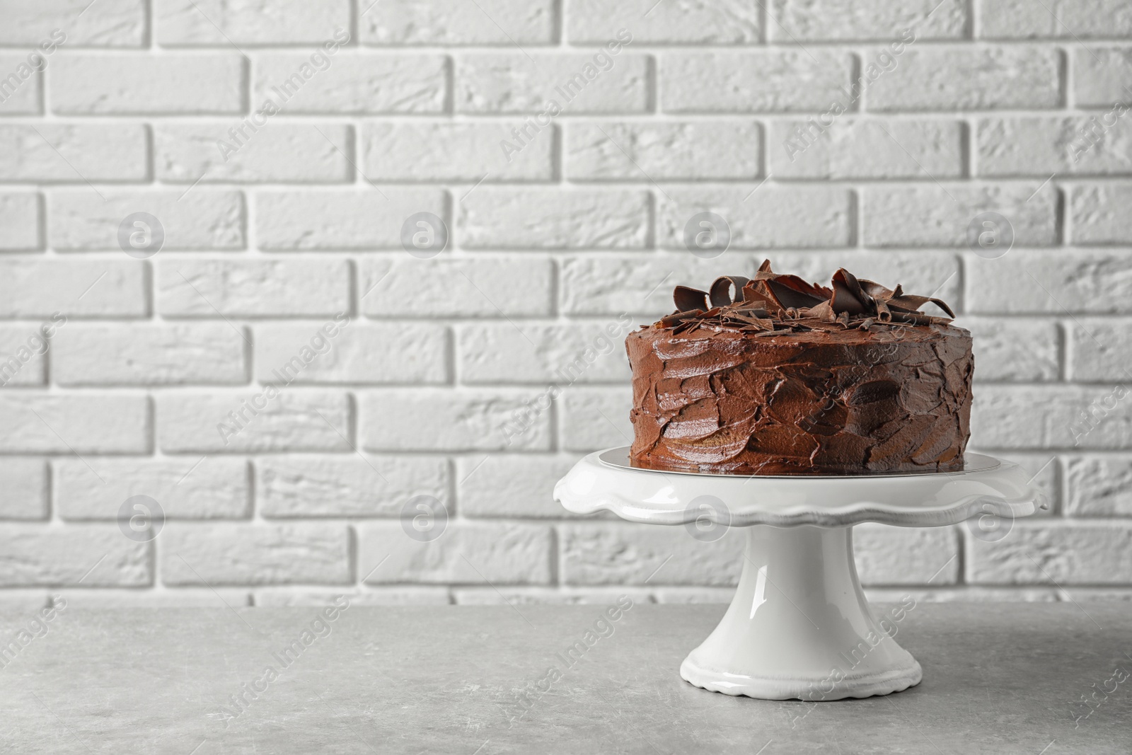 Photo of Stand with tasty homemade chocolate cake on table near brick wall. Space for text