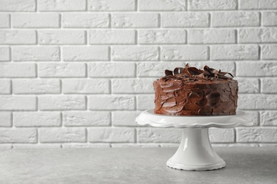 Photo of Stand with tasty homemade chocolate cake on table near brick wall. Space for text