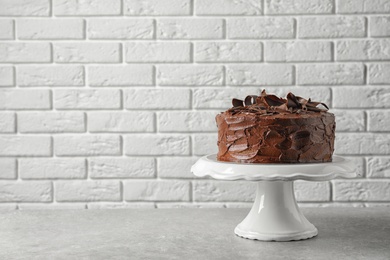 Stand with tasty homemade chocolate cake on table near brick wall. Space for text