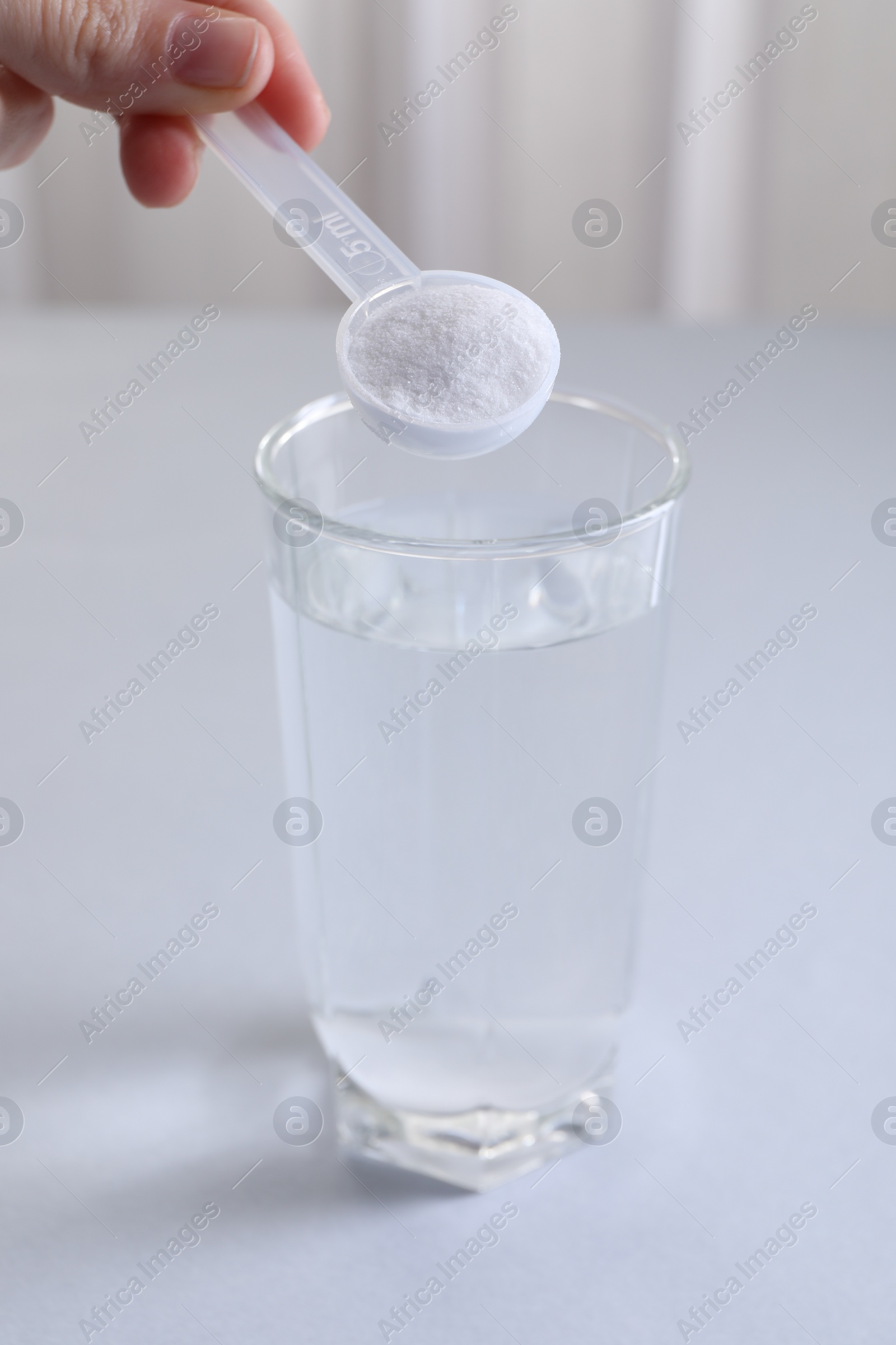 Photo of Woman adding baking soda into glass of water at white table, closeup