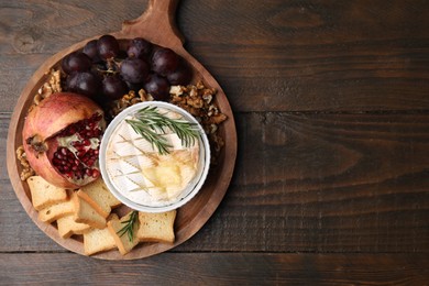 Board with tasty baked camembert, croutons, grapes, walnuts and pomegranate on wooden table, top view. Space for text