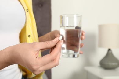 Photo of Woman with pill and glass of water indoors, closeup