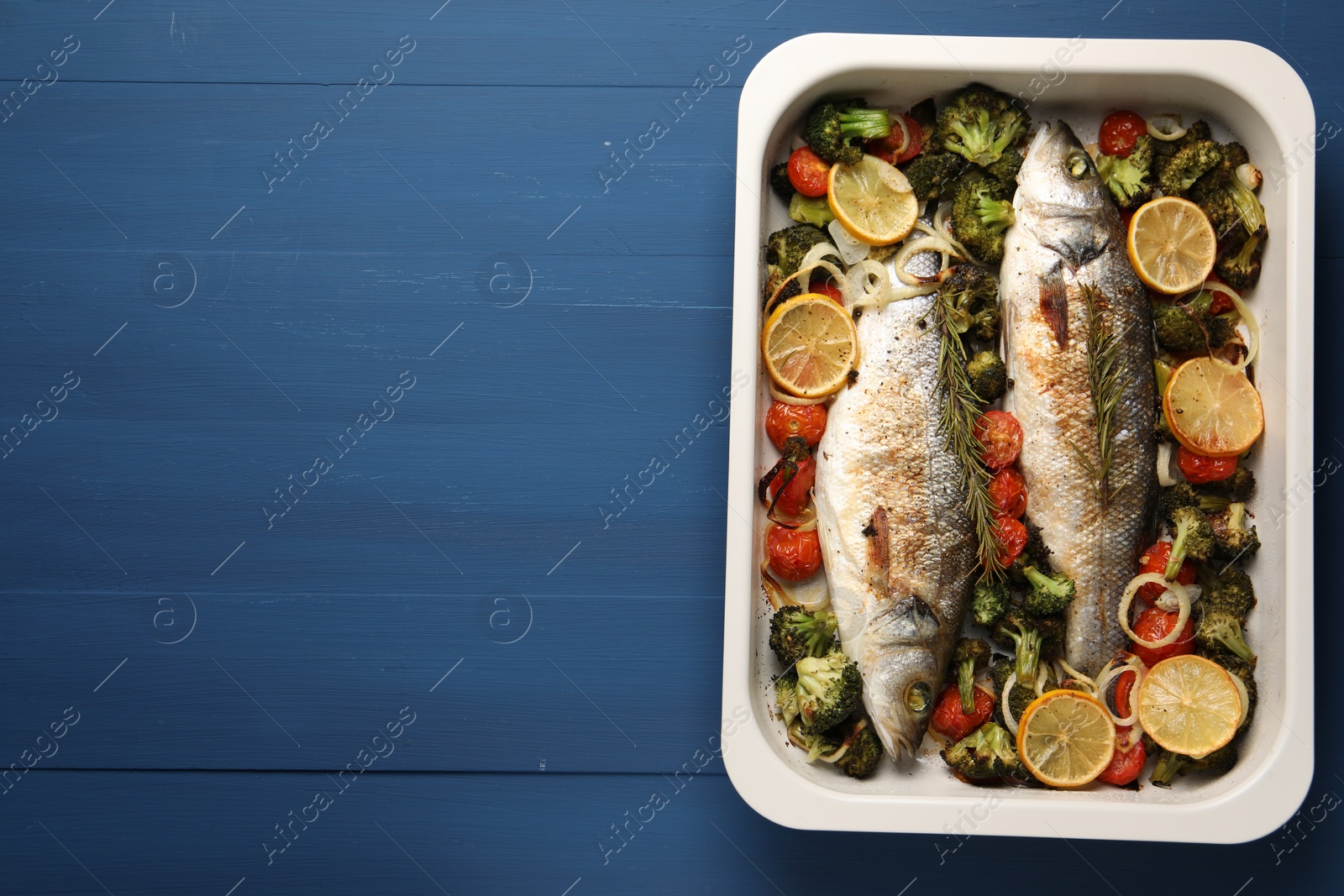 Photo of Delicious fish with vegetables and lemon in baking dish on blue wooden table, top view. Space for text