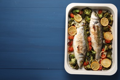 Delicious fish with vegetables and lemon in baking dish on blue wooden table, top view. Space for text