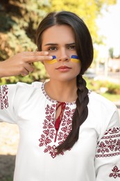 Sad young woman with drawings of Ukrainian flag on face in park