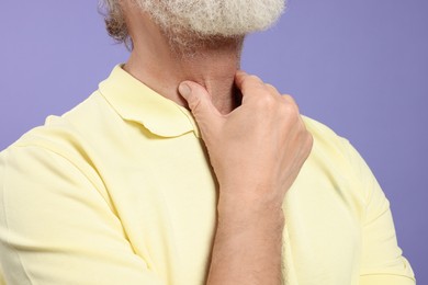 Photo of Senior man suffering from sore throat on light purple background, closeup. Cold symptoms